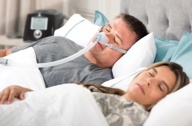 Adult sleeping peacefully with a CPAP nasal pillow mask, in soft morning light