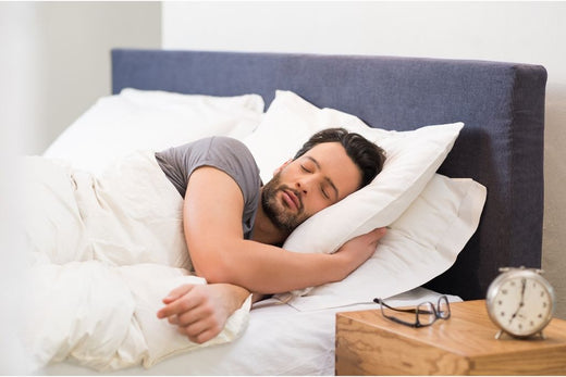 A man sleeping in his bed next to an alarm clock