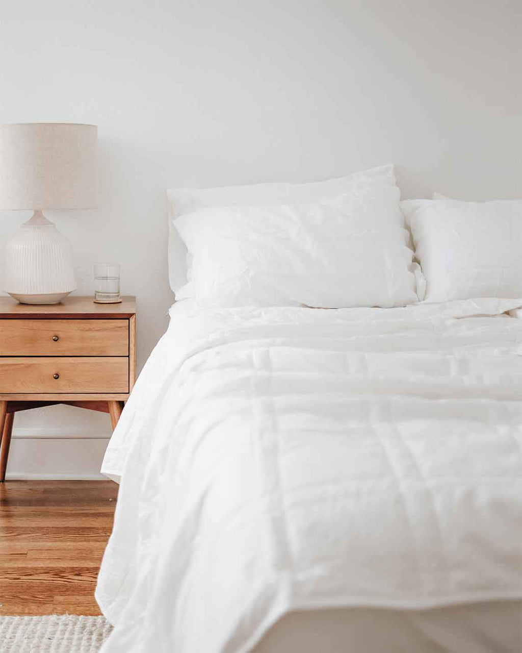 White Baloo weighted comforter layered on a bed next to a wood nightstand and lamp