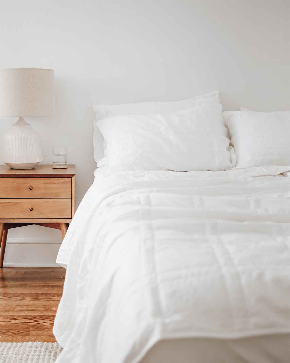 White Baloo weighted comforter layered on a bed next to a wood nightstand and lamp