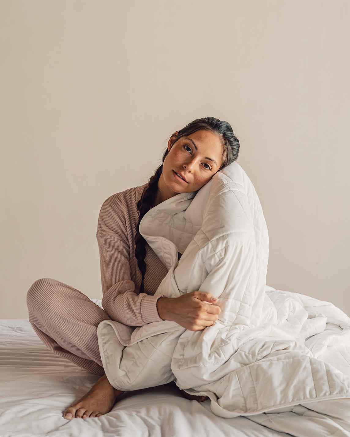 Woman sitting cross-legged on a bed hugging the quilted Baloo weighted comforter