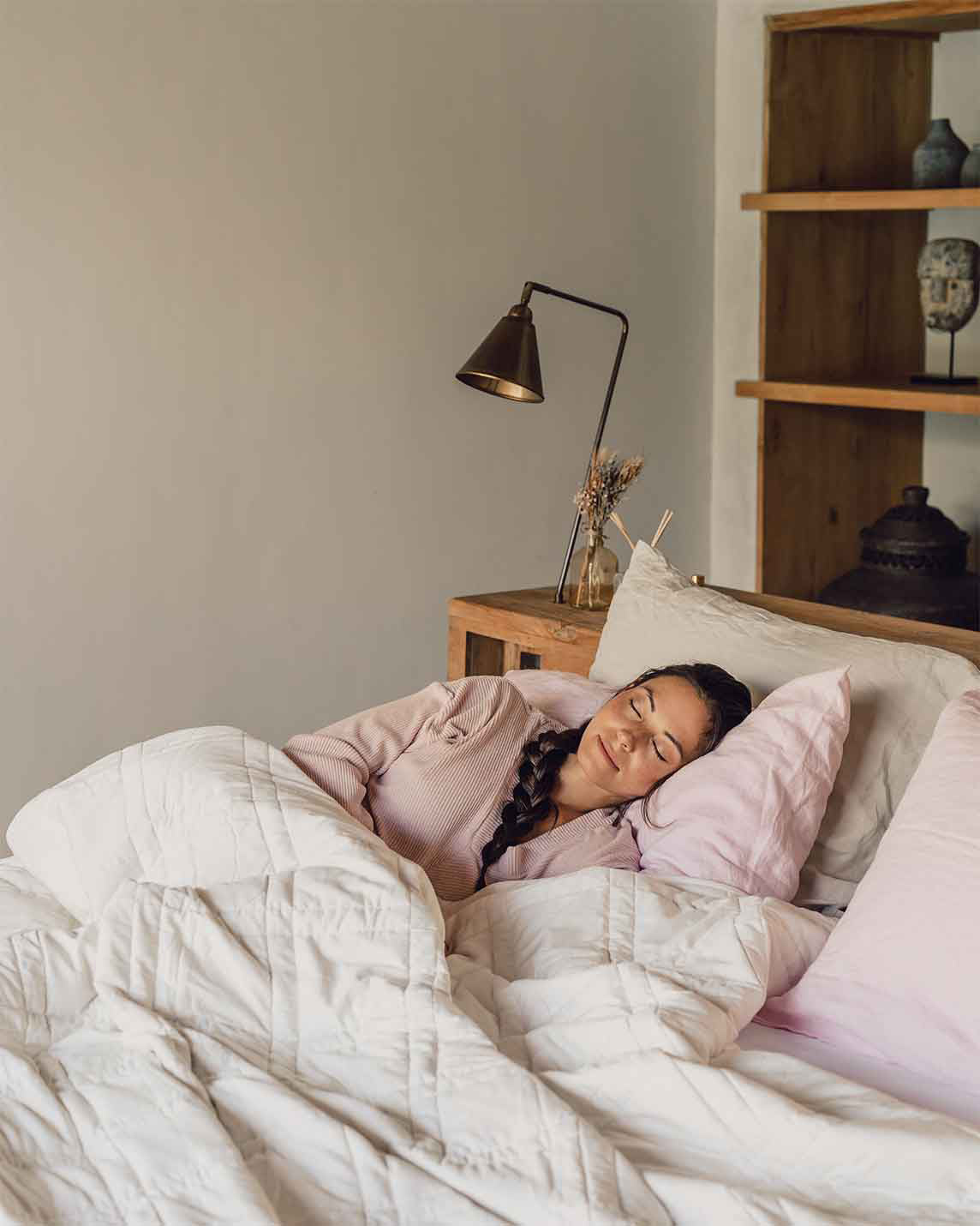 Woman resting on a pink pillow beneath the white Baloo weighted cotton comforter