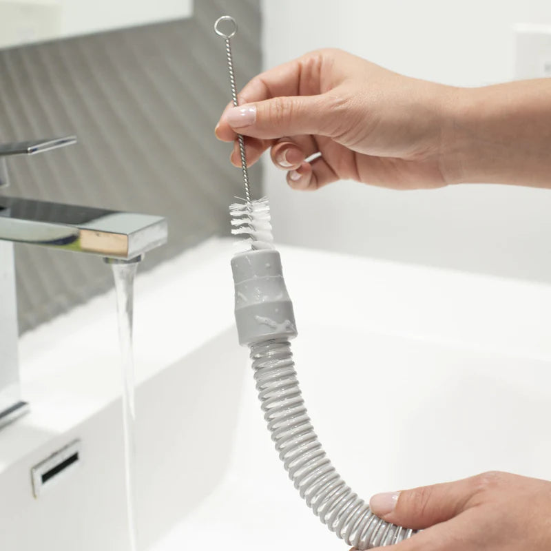 Hands scrubbing a CPAP hose with a long tube cleaning brush under running faucet water