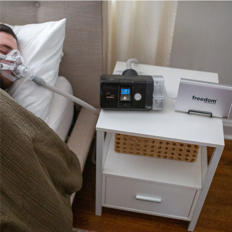 Freedom 160 CPAP Battery Backup placed on a nightstand next to a CPAP machine