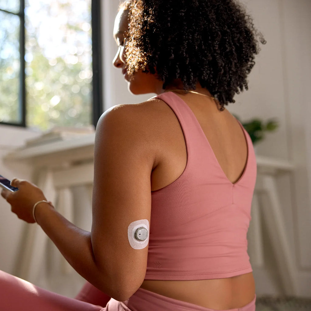 Woman on a fitness mat holds her phone, Dexcom Stelo biosensor on the back of her upper arm