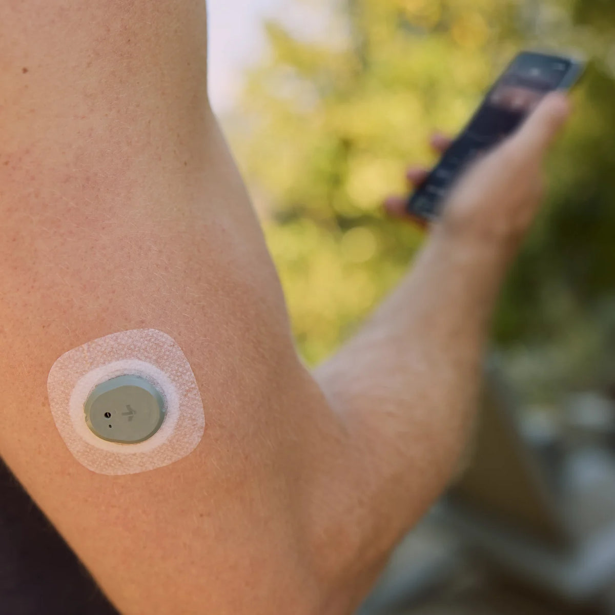 Close-up of the Dexcom Stelo biosensor on the upper arm with the Stelo app open on a phone