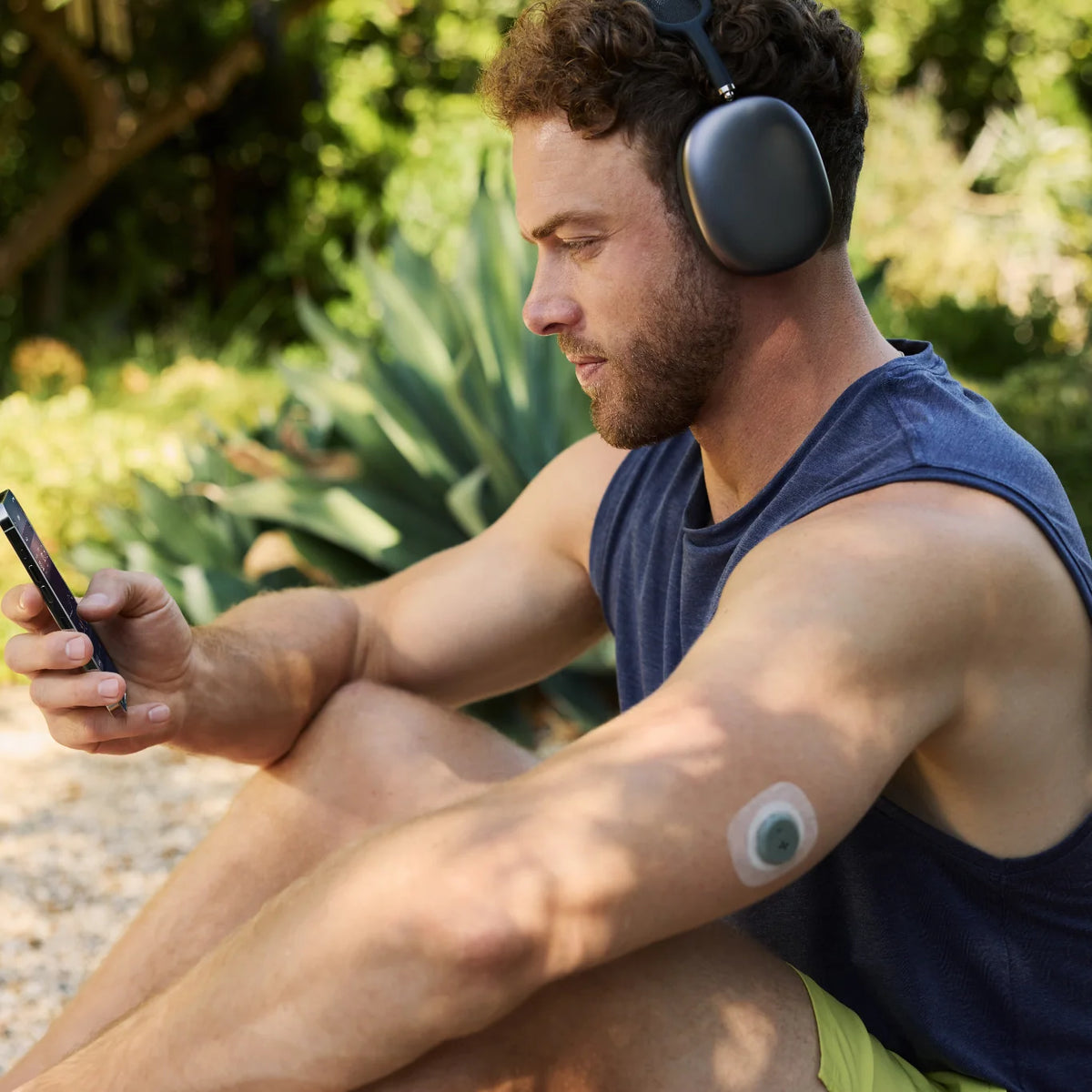 Man in headphones checks the Stelo app on his phone while wearing a Dexcom Stelo biosensor on his arm
