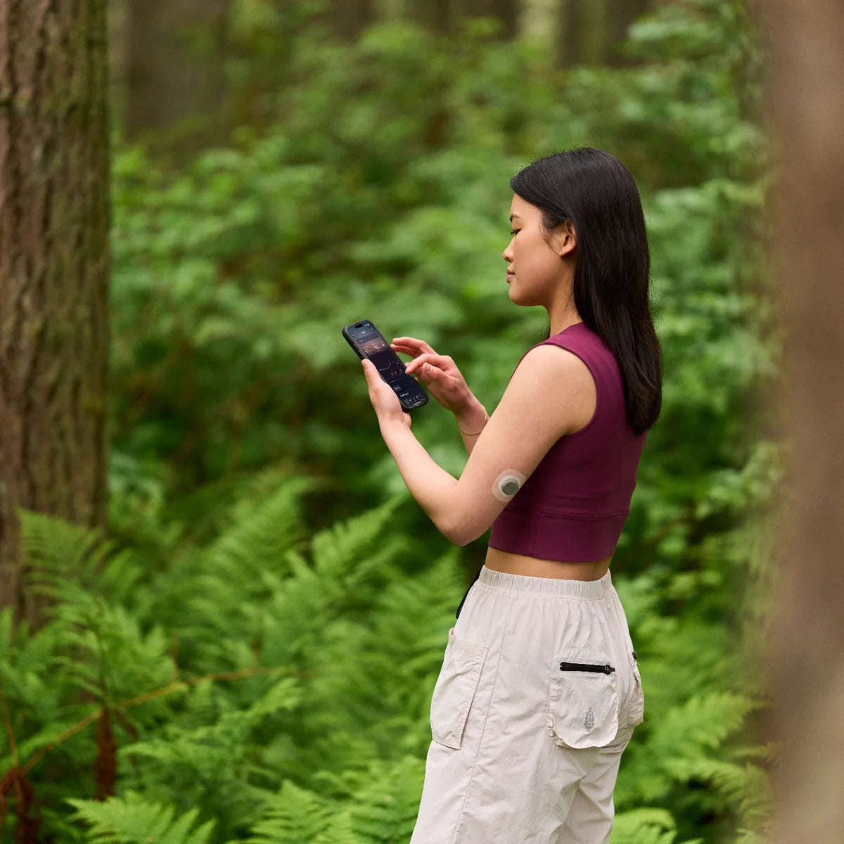 Woman on a forest trail checks glucose on her phone while wearing the Dexcom Stelo biosensor