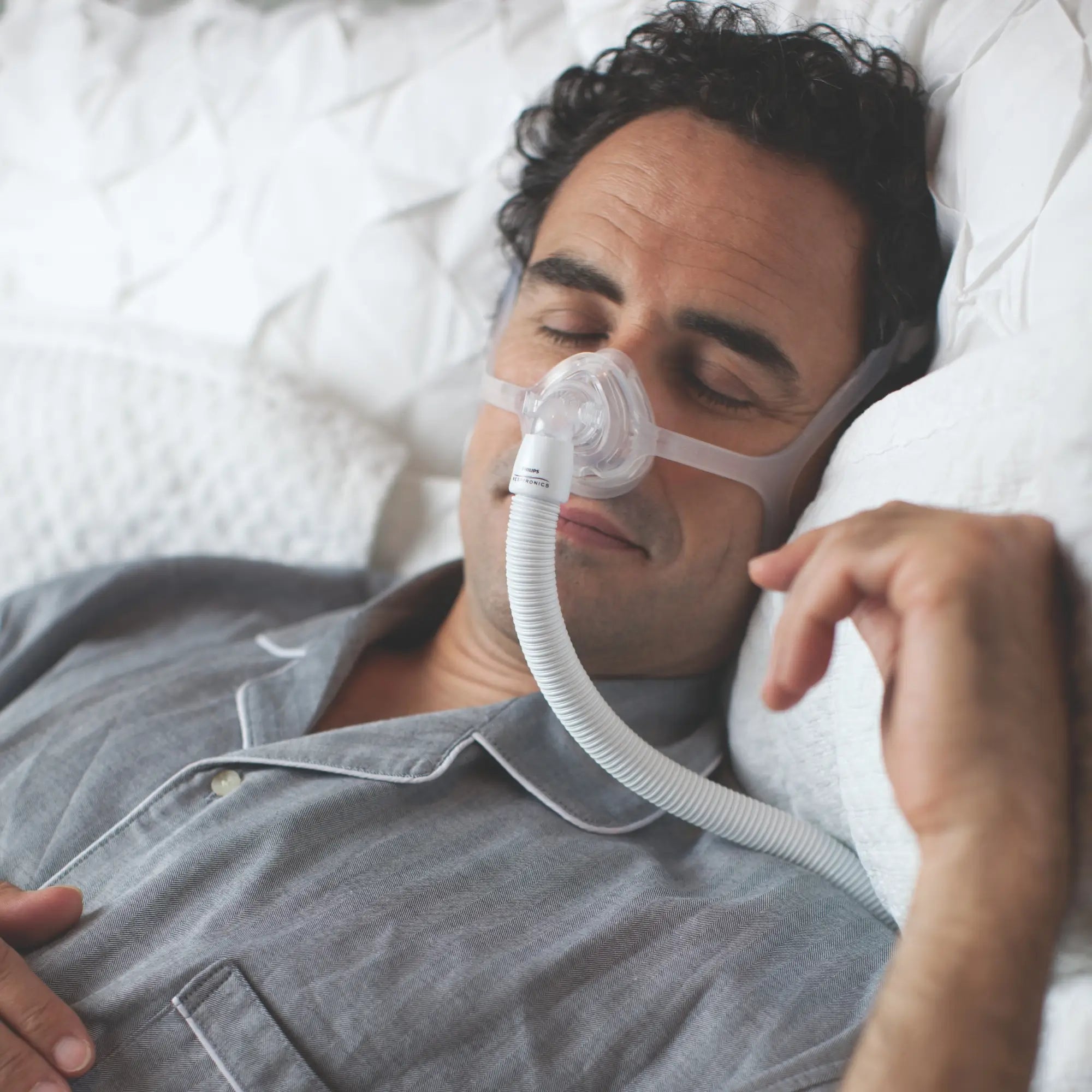 Man sleeping in bed wearing Philips Respironics Wisp nasal CPAP mask with clear frame