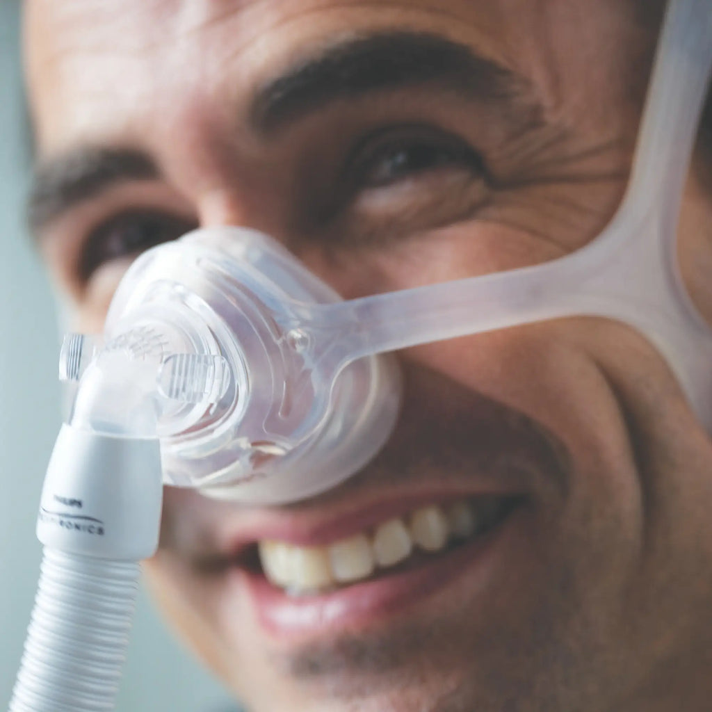 Close-up of smiling man wearing Philips Wisp nasal CPAP mask with clear frame and tubing