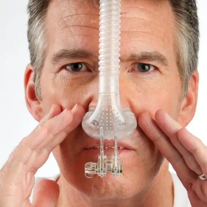 Man holding myTAP PAP nasal pillow CPAP mask to his nose, showing moldable oral mouthpiece that replaces headgear straps