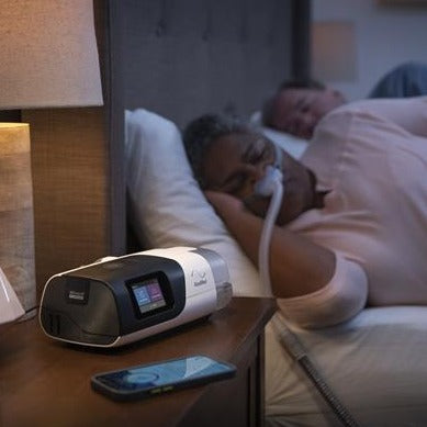 Couple sleeping at night beside ResMed AirSense 11 CPAP machine glowing on the nightstand