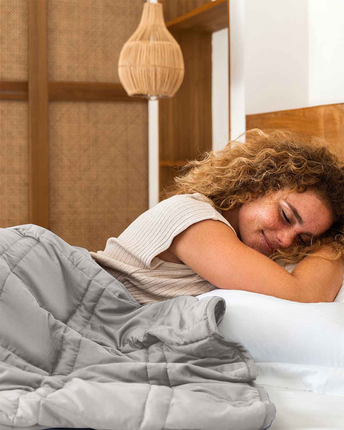 Woman smiling while sleeping under the gray Baloo weighted cotton comforter in bed