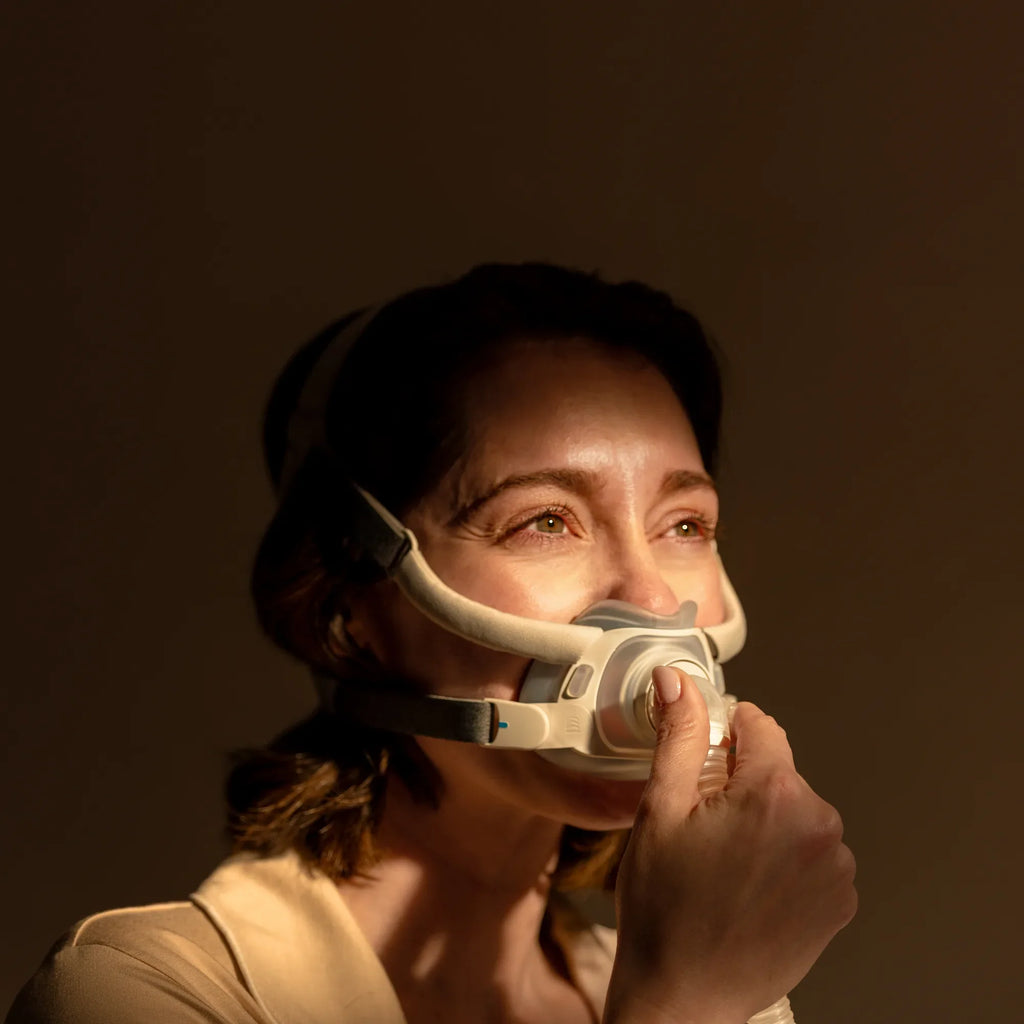 Woman putting on the ResMed AirTouch F40 full face mask at night