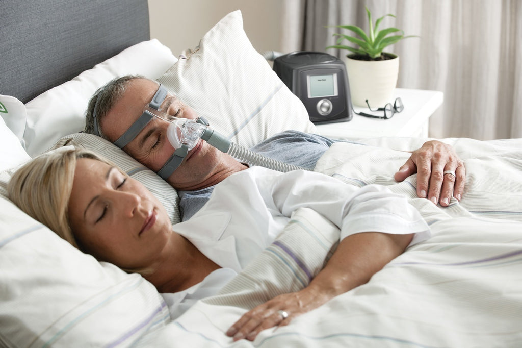 Male sleeping with women on the side and using the clear Eson Nasal Mask with grey headgear by Fisher and Paykel.