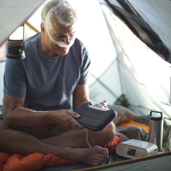 Man using the Respironics white travel battery to power the DreamStation CPAP Machine