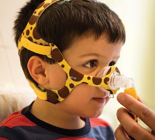 Hand adjusting boy's Wisp Pediatric Nasal Mask with giraffe print.