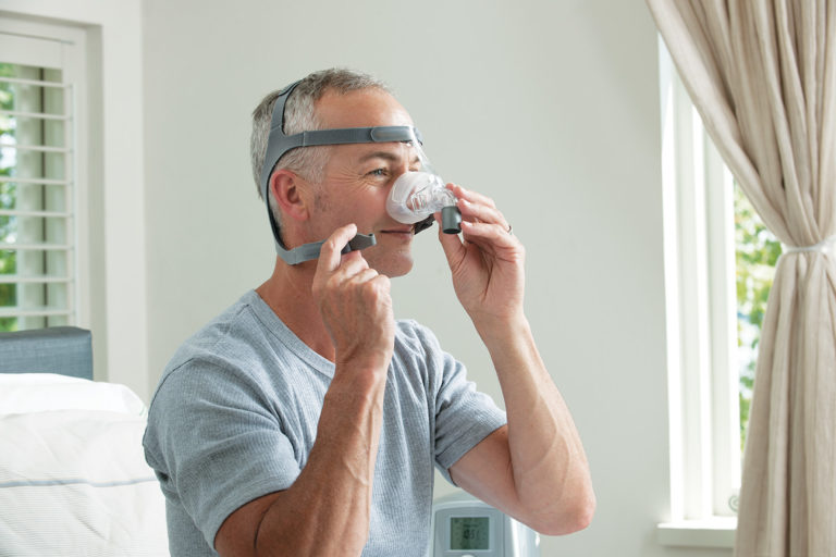 Man adjusting headgear clips of the clear Eson Nasal Mask by Fisher and Paykel.