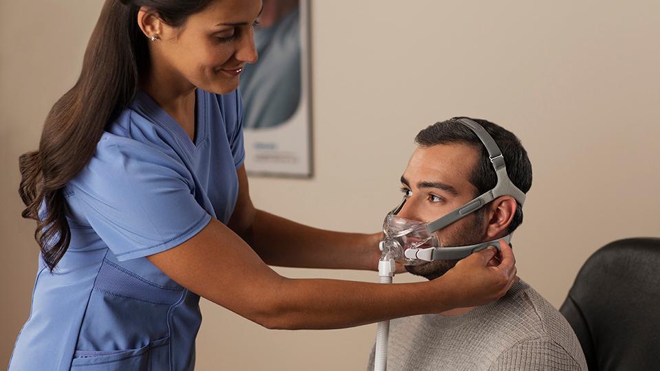 Nurse fitting the Respironics Amara mask to the man sitting in front of her