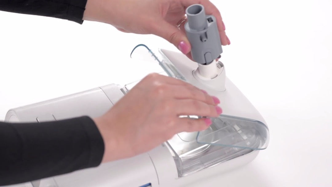 Woman installing the grey SoClean adapter and diffuser connection to the Respironics DreamStation System One.